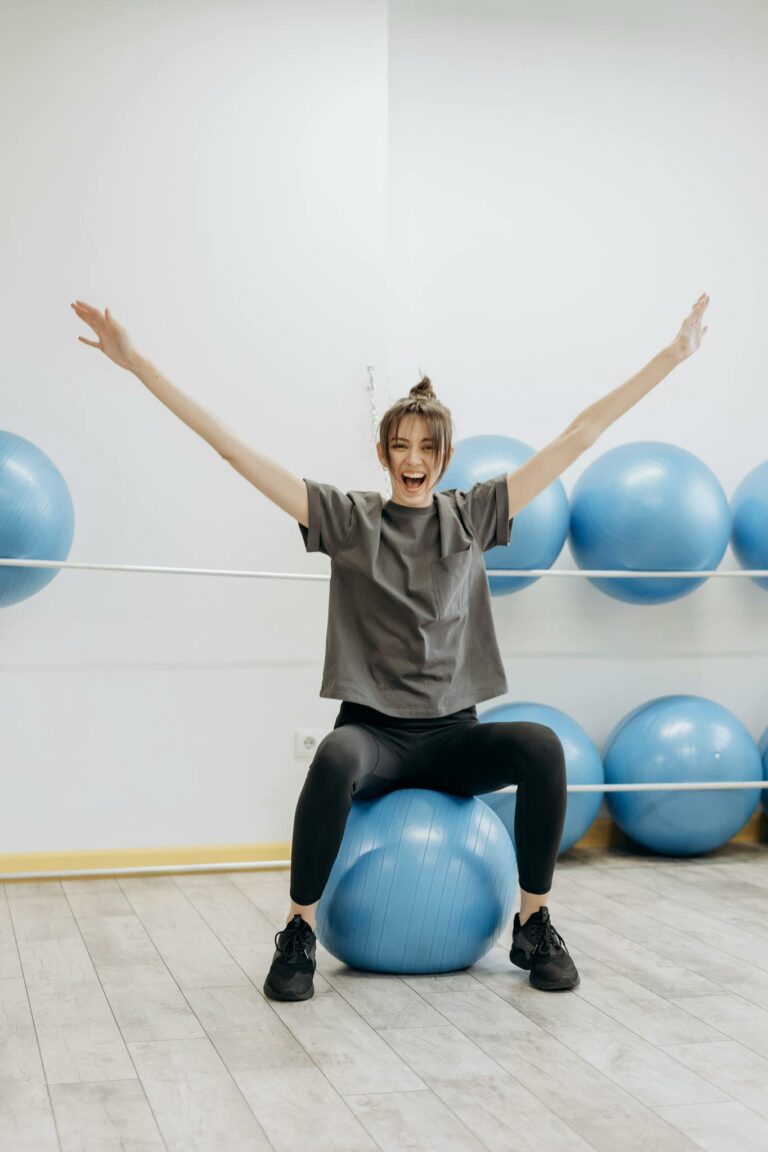 A cheerful woman in active wear exercises with a yoga ball indoors, promoting wellness.