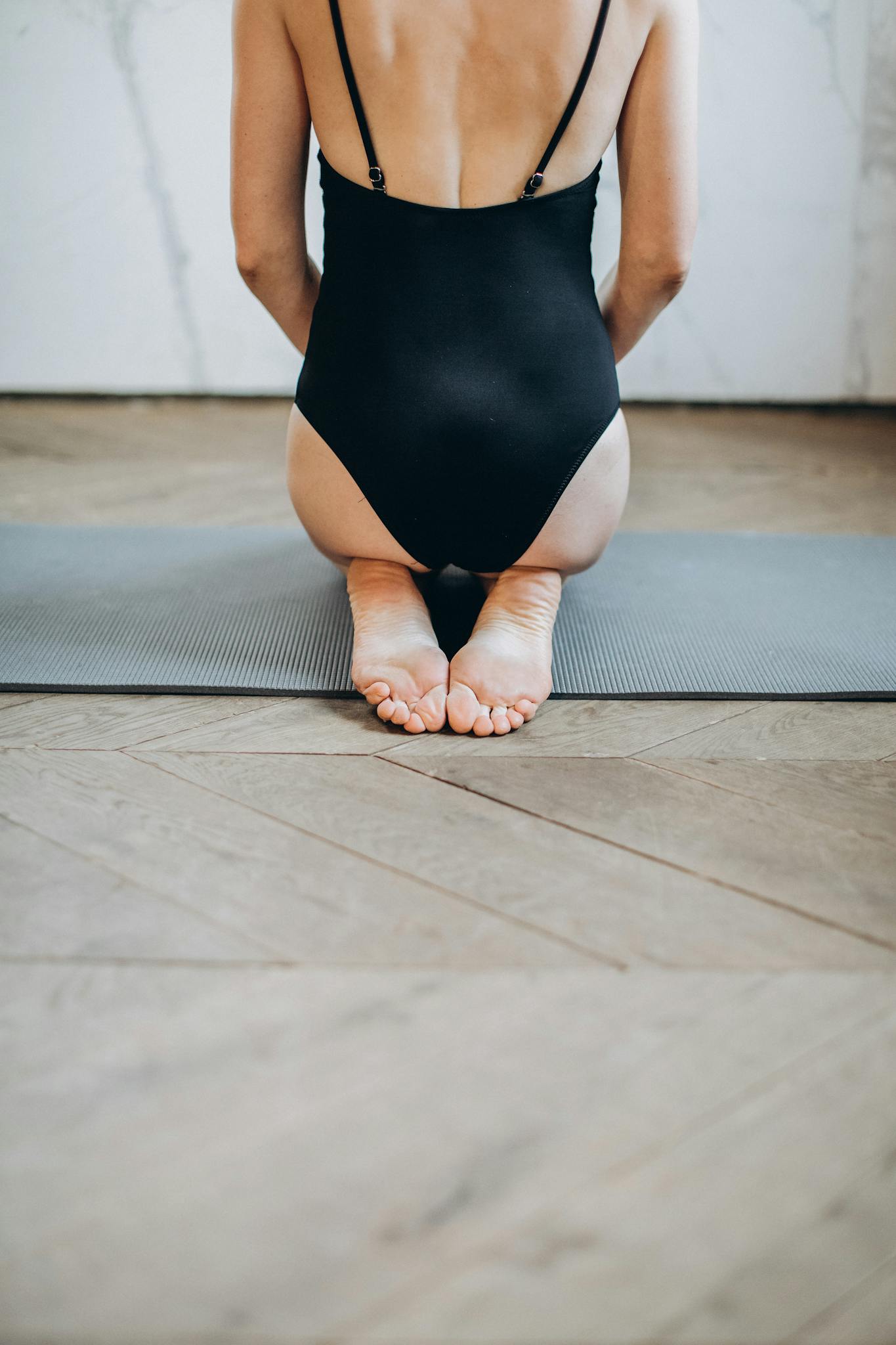 Back view of woman in swimsuit performing yoga on mat.